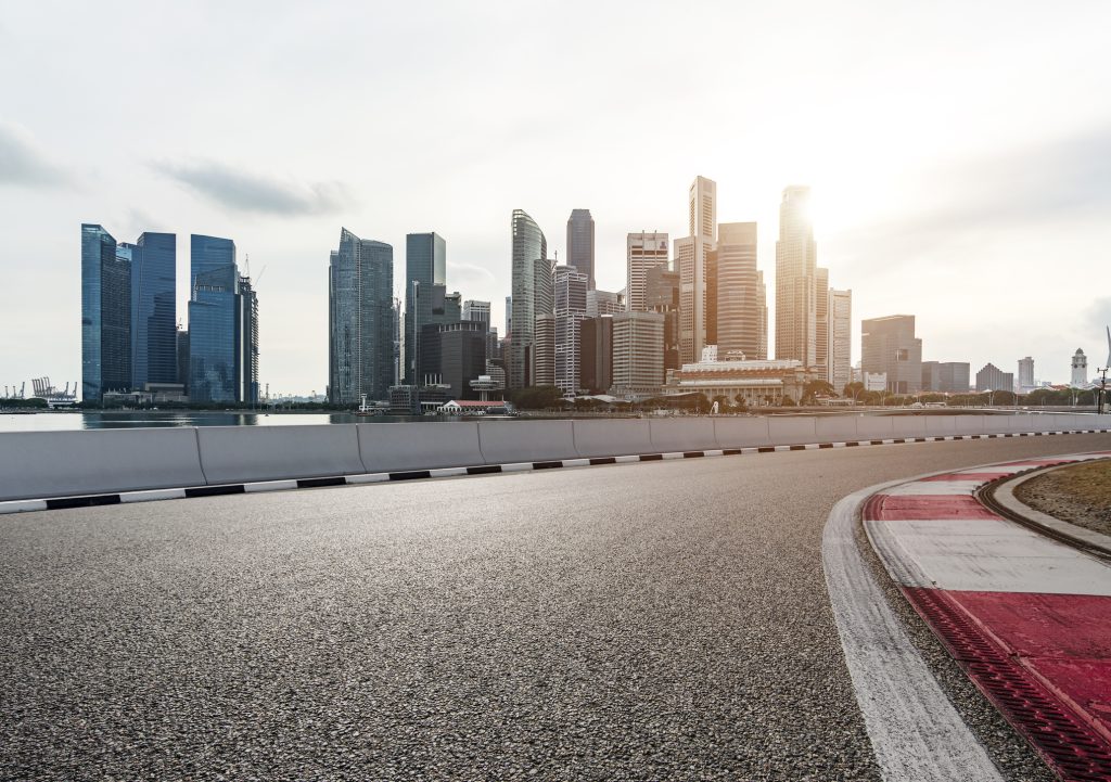 View from a racetrack with red and white curbs on the right leading towards a modern city skyline across a body of water.