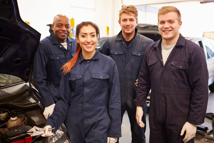 Four students in automotive training smile as they stand next to an EV