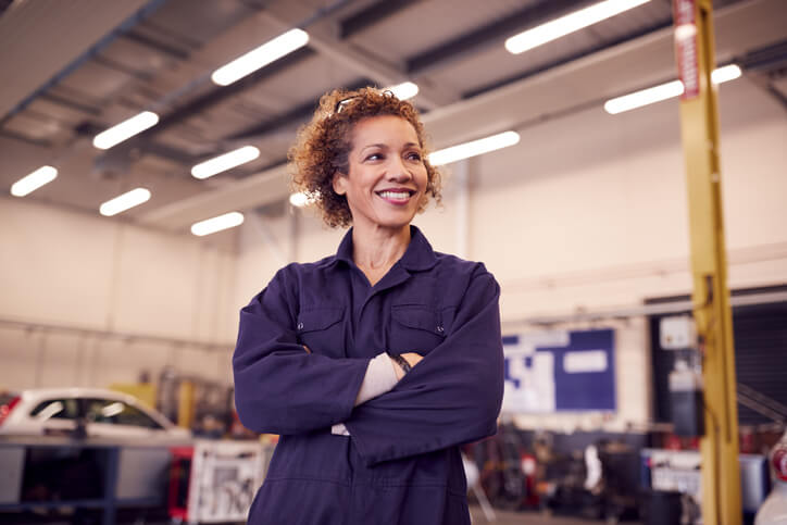 Female auto mechanic wearing googles and standing in an auto repair shop after auto mechanic school