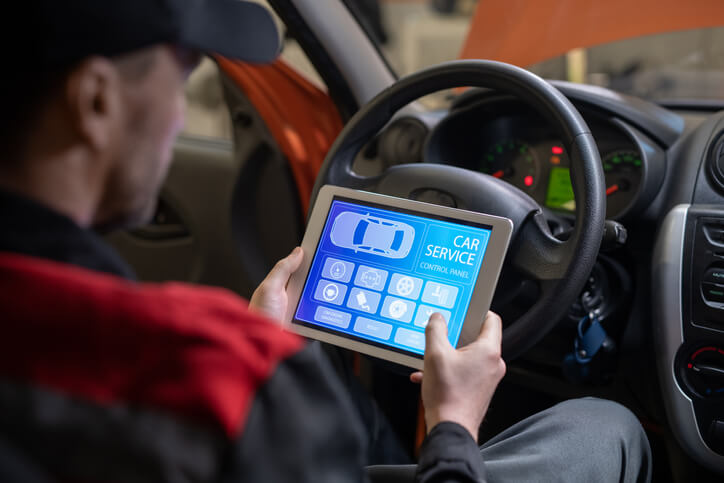 An auto mechanic using auto repair software in a car after auto mechanic school.