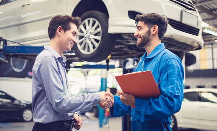 A service advisor training grad shaking hands with a car owner in a garage.