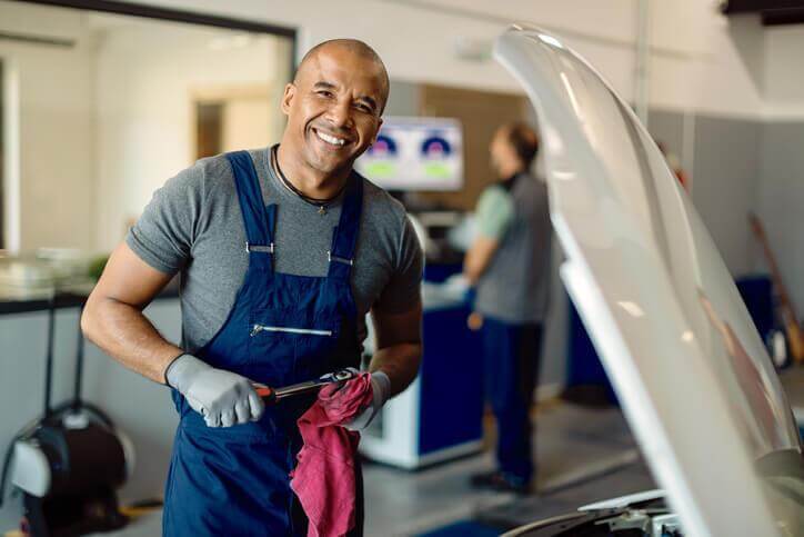 A smiling male auto mechanic in a repair shop after automotive school