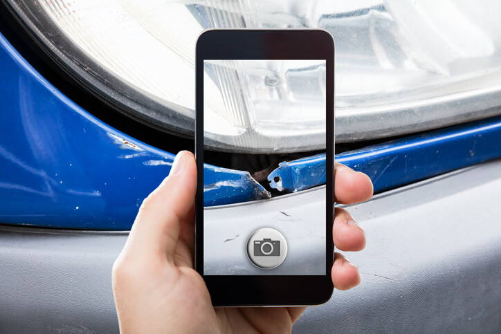 A male auto body estimator taking a picture of a damaged car