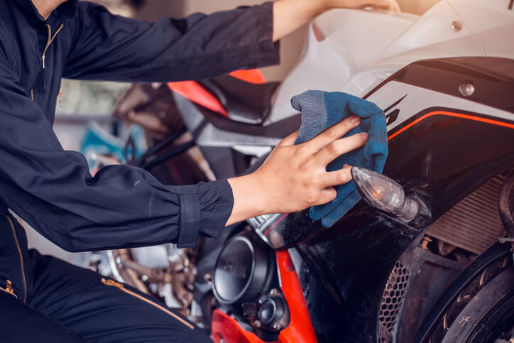 An Auto Detailing Training graduate applying lubricant to a car's surface to reduce friction and protect the paintwork