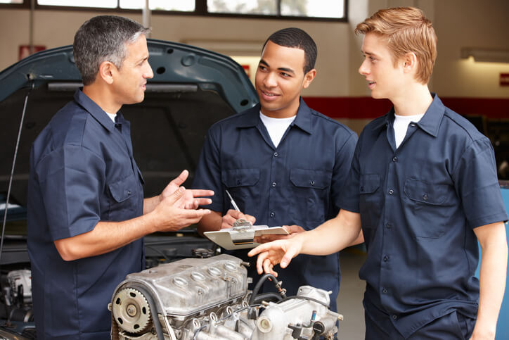 A male auto mechanic communicating with his apprentices after completing his automotive training