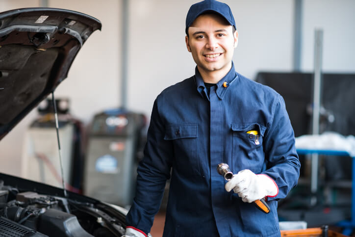 A smiling male auto mechanic working on a vehicle after completing his automotive training