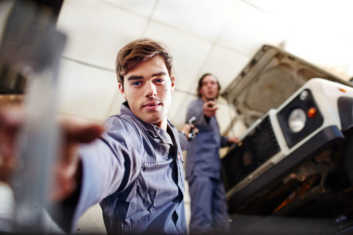 An automotive training student working with an instructor in a garage setting