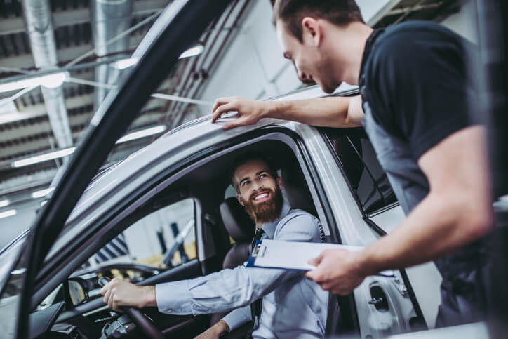 A collision estimating training grad talking to a customer in a car.