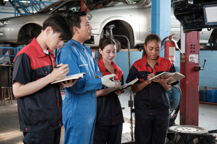 An experienced shop foreman training a group of apprentices who have recently completed auto mechanic school