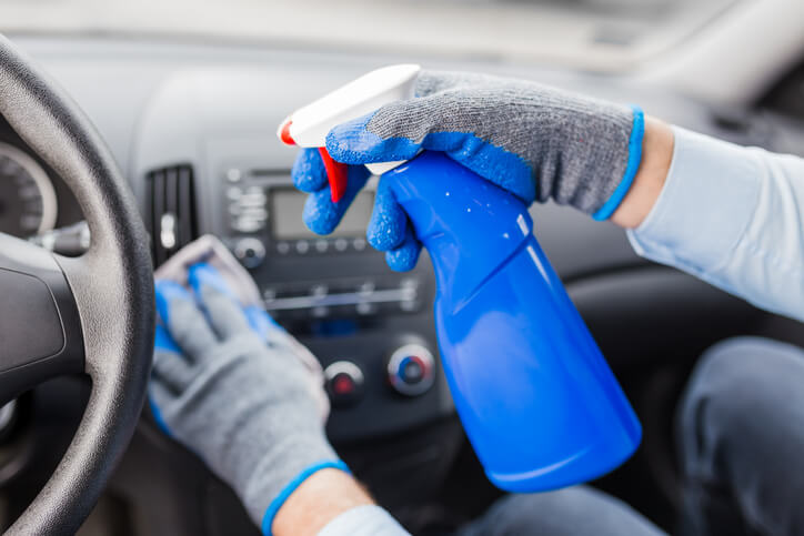 An auto detailer cleaning a car’s interior with a specialized auto detailing spray bottle after completing his auto detailing training