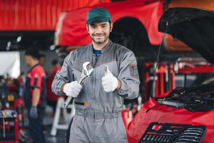 A new worker hired to become a mechanic posing in a shop holding a wrench