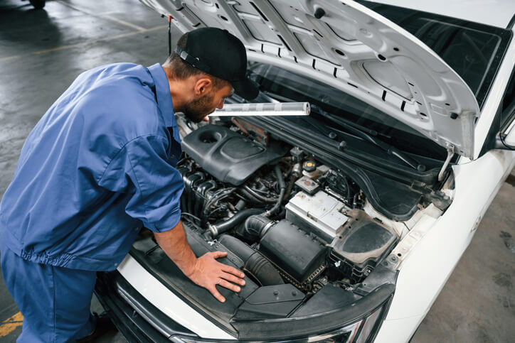 A focused engine technician diagnosing a vehicle engine after graduating from auto mechanic school