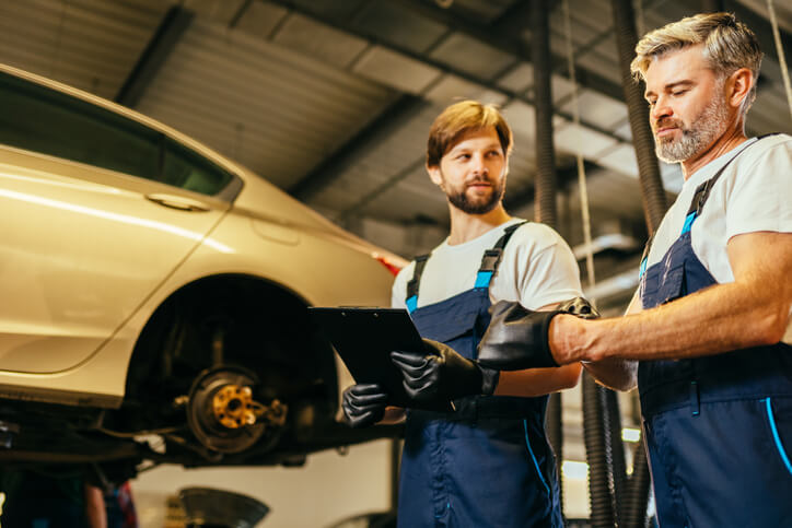 A male hybrid and electric vehicle mechanic interacting with his apprentice at an auto repair shop