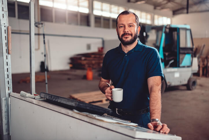 An auto mechanic training grad working in a shop at the computer holding a mug