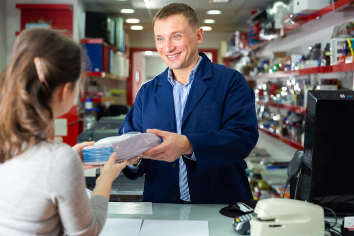 A smiling male auto parts manager handing a package to a female customer after completing his auto parts training