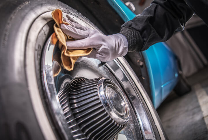 A male auto detailing professional cleaning a vintage wheel