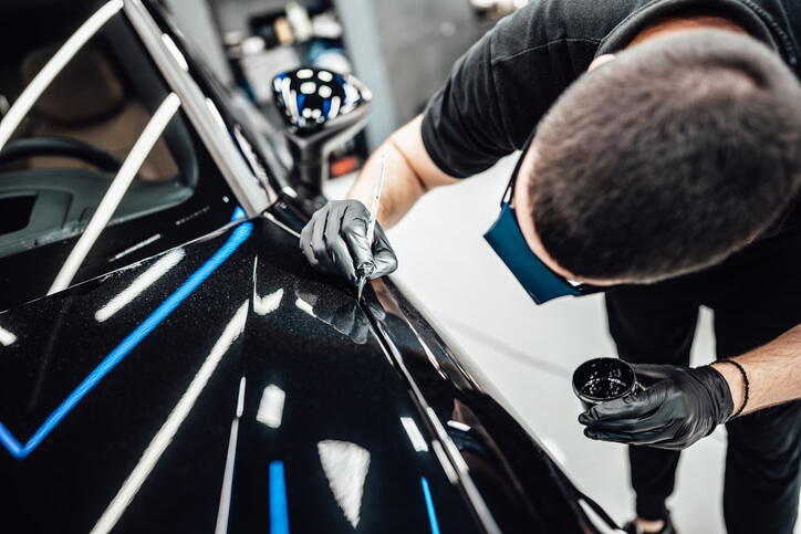 A male auto detailer applying light paint on a car’s surface after auto detailing training