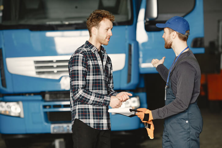 A male driver recruiter interacting with an experienced truck driver at a warehouse after dispatch training