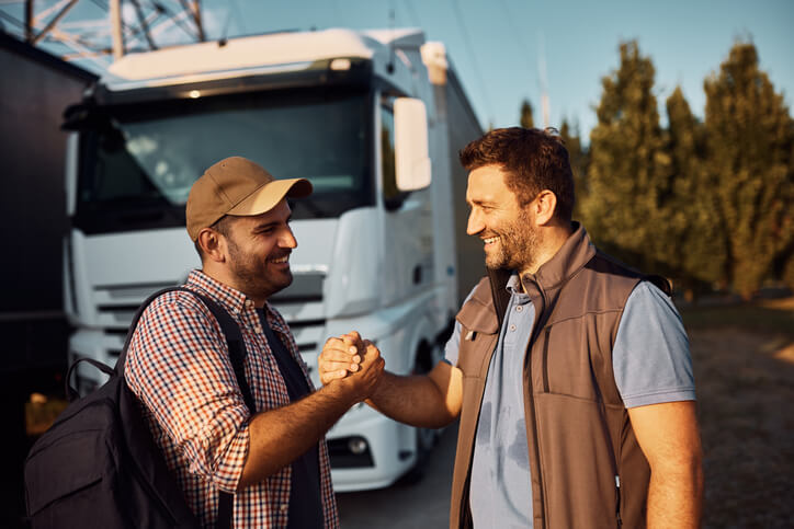 A happy driver recruiter shaking hands with a truck driver at a warehouse after dispatch training