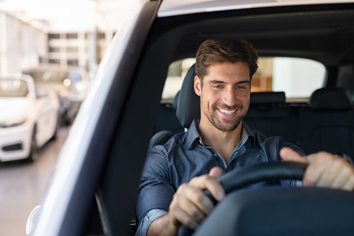 A smiling man driving an EV on a highway after graduating from automotive school