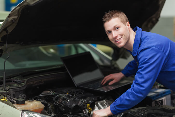 A male auto mechanic diagnosing and repairing a vehicle with the aid of technology after completing auto mechanic training