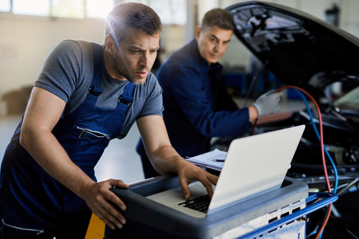 A pair of auto mechanic workers troubleshooting on a laptop