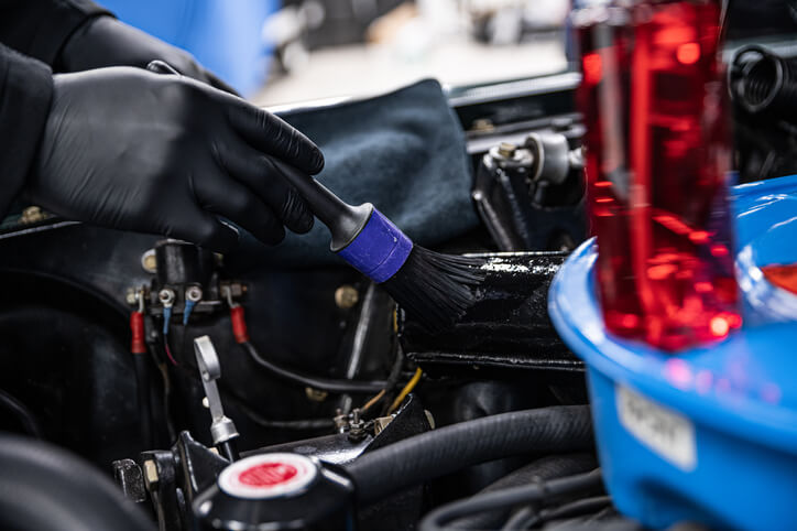 A male auto detailing professional cleaning a vehicle’s engine with a brush after auto detailing training