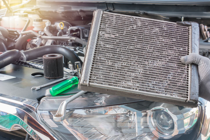 An auto mechanic holding a vehicle’s radiator in a repair shop after automotive school