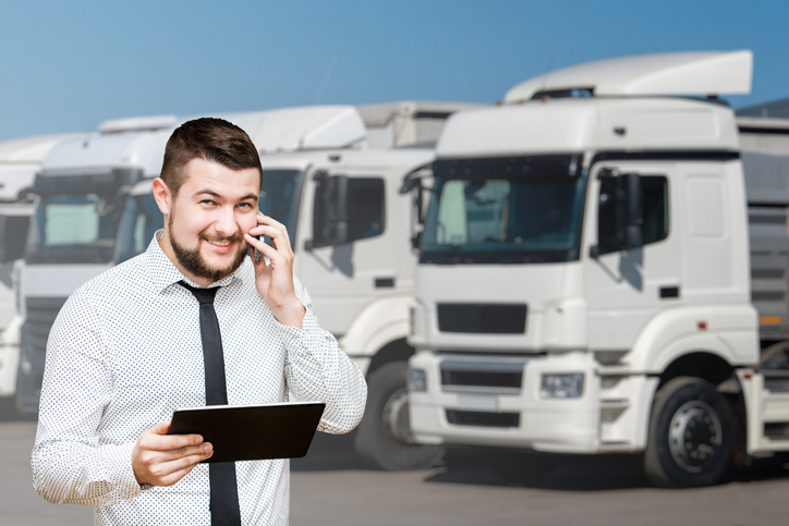 Composed male dispatcher speaking on his cell phone in front of trucks after dispatch training