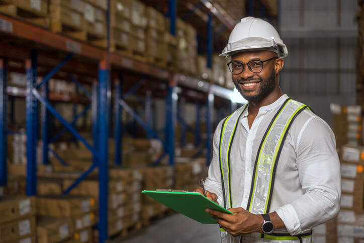 A smiling logistics manager checking inventory at a warehouse after completing his dispatch training