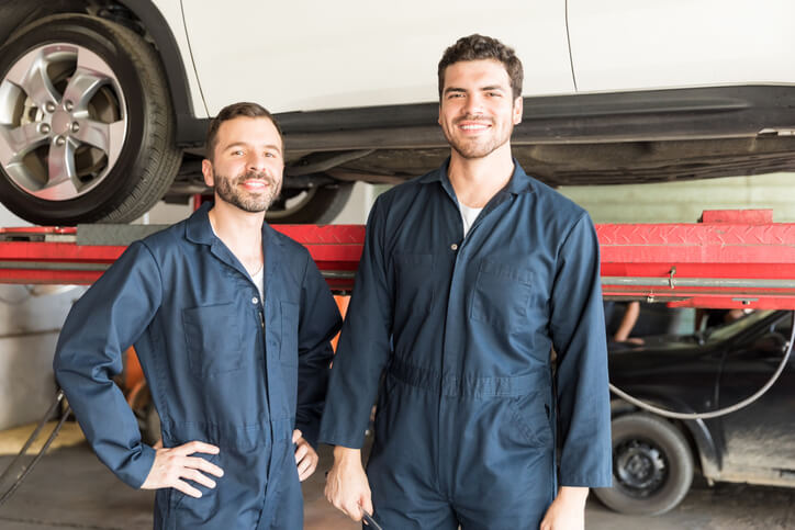 A pair of smiling auto parts specialists taking a photo at a workshop after their auto parts training