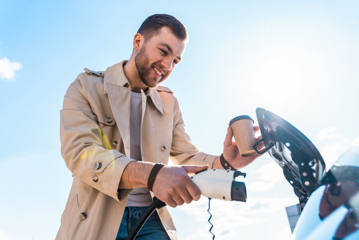 A happy mechanic charging an EV at a home charging station after completing his automotive training