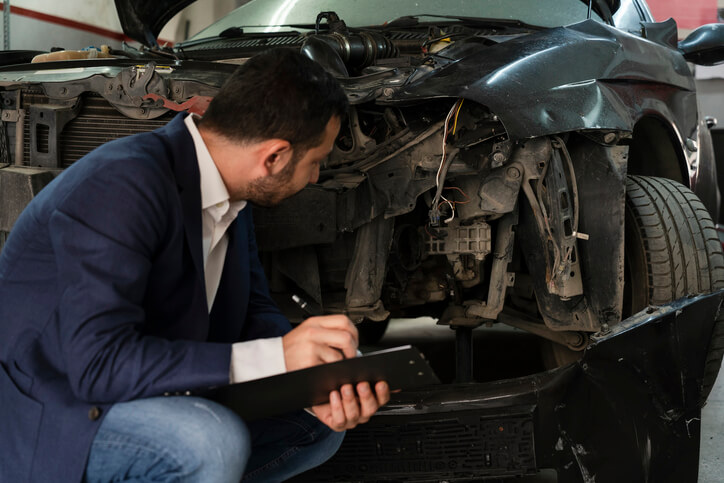 A male collisions estimator estimating the salvage value of a damaged vehicle after completing his auto body training