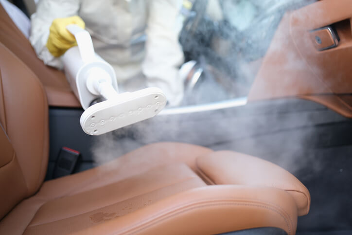 An auto detailing grad steam cleaning a car’s leather interior