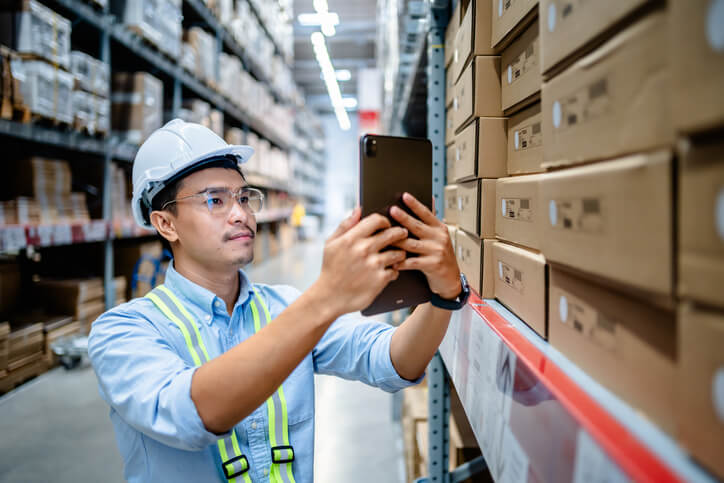 An auto parts training grad looking at his tablet for a code for an auto part on warehouse shelves