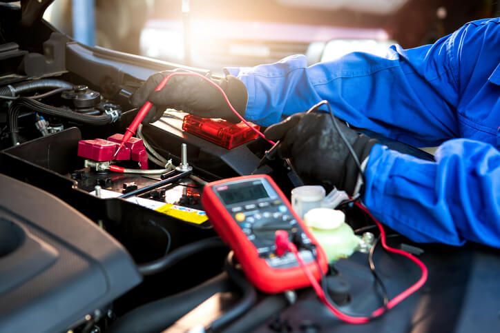 A male hybrid and electric vehicle mechanic working with a multimeter