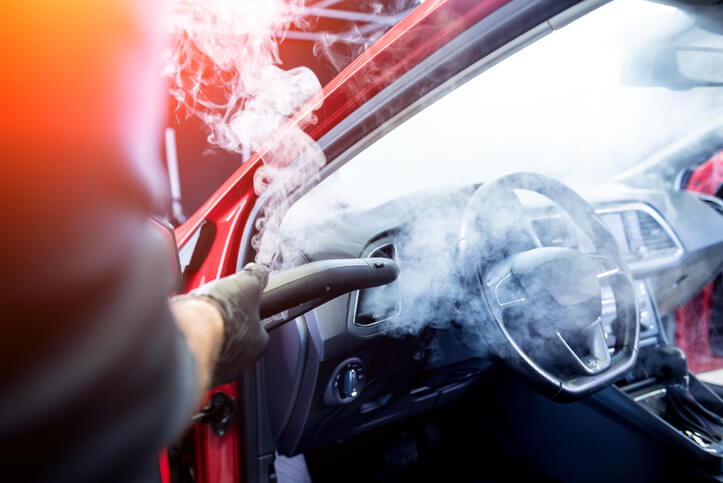 An auto detailing grad steam cleaning a red car