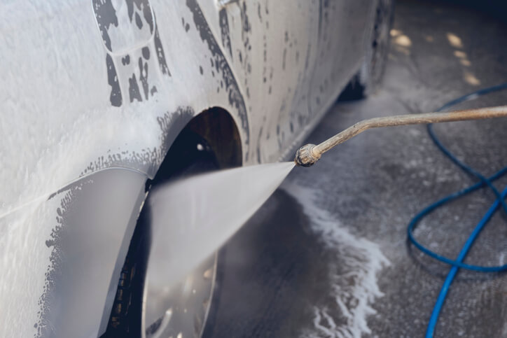 A male auto detailing professional holding a high-pressure water sprayer for car washing