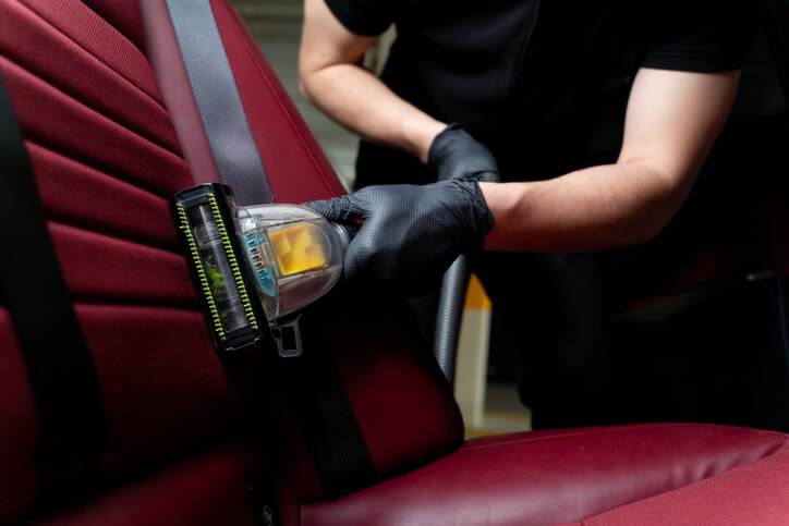 A male auto detailing professional detailing a car’s backseat with the help of a hoover and turbo brush nozzle