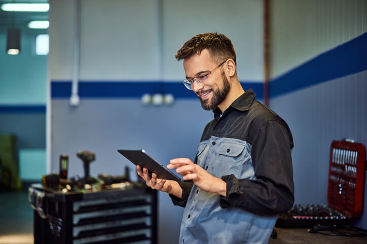 A smiling male auto mechanic holding a tablet at a repair shop after graduating from auto mechanic school