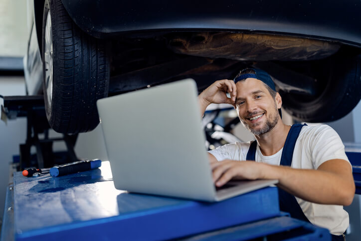 An auto mechanic training grad doing admin tasks on a laptop in a shop