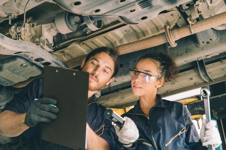 A female automotive technician working on a vehicle alongside an instructor