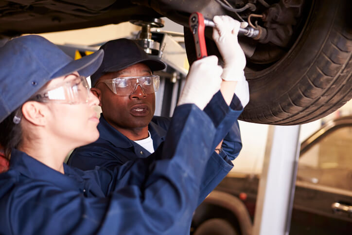 A female automotive technician with another technician working on the underbody of a vehicle