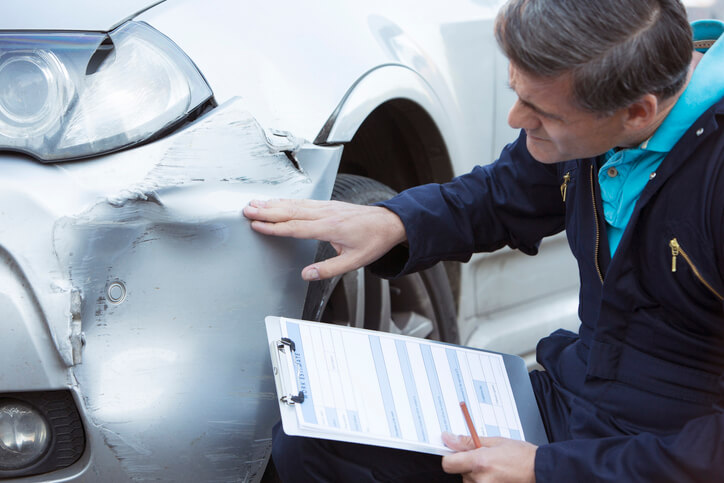 A male auto mechanic inspecting a damaged car and filling in repair estimates after his collision estimating training