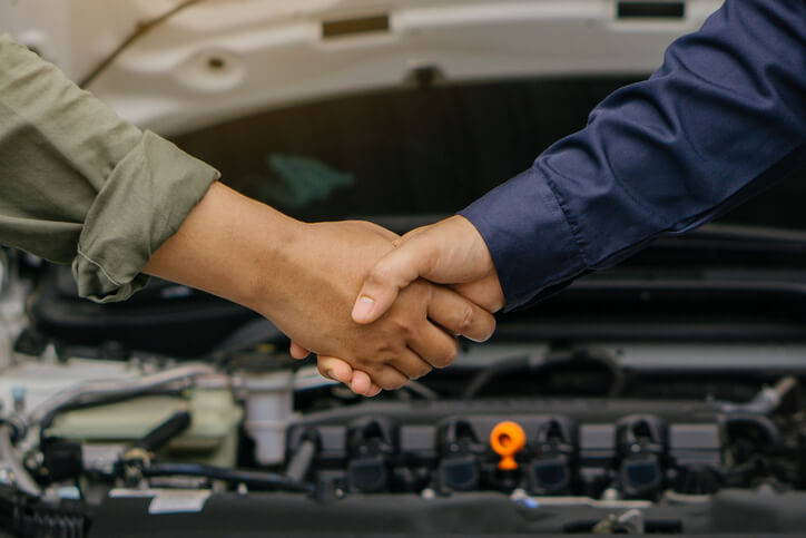 An auto mechanic shaking hands with a customer after graduating from auto mechanic school