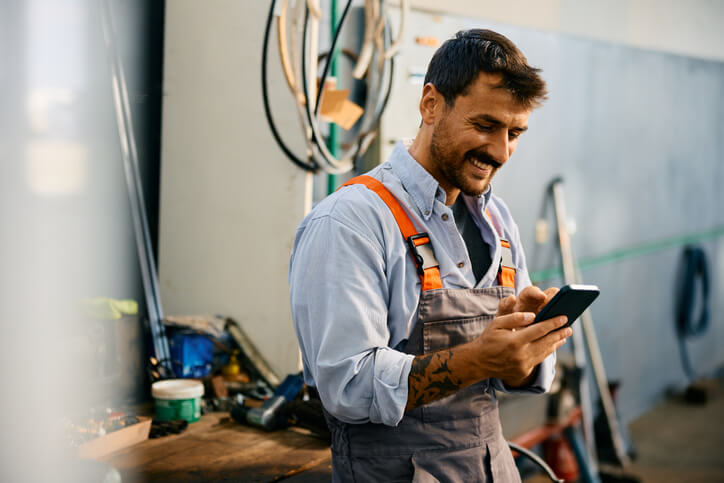 A happy male mechanic using an auto repair app in a garage after completing his auto mechanic training