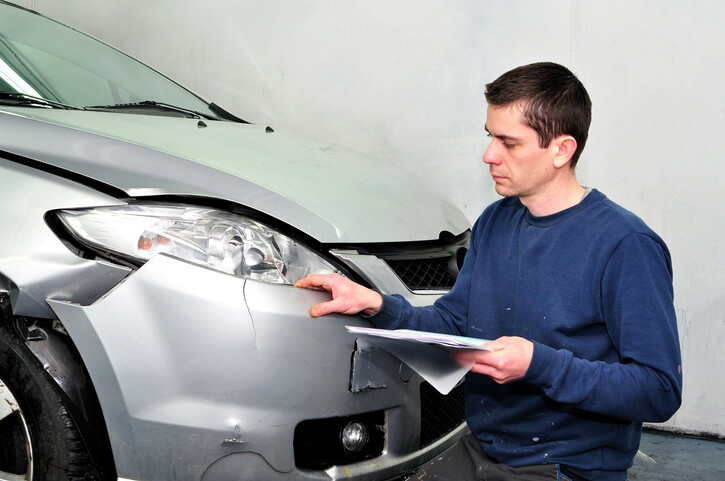 A male auto mechanic inspecting the damage to a car after his collision estimating training