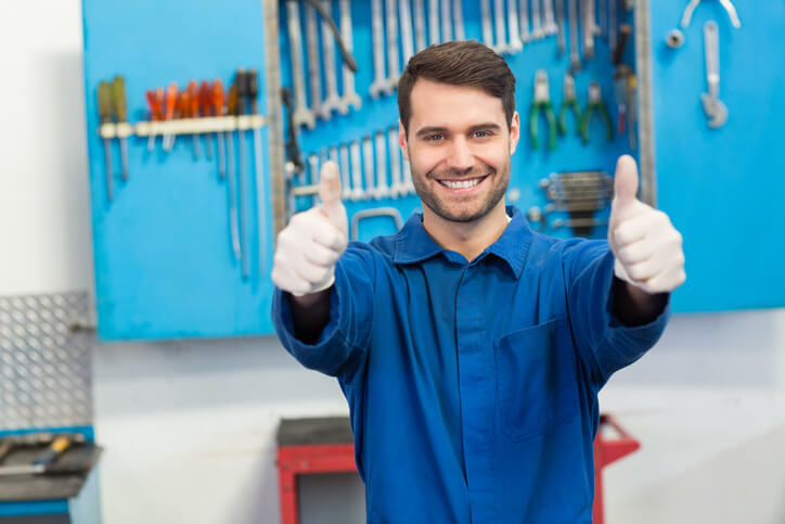 A smiling auto mechanic working on a vehicle in a repair shop after completing his auto mechanic training