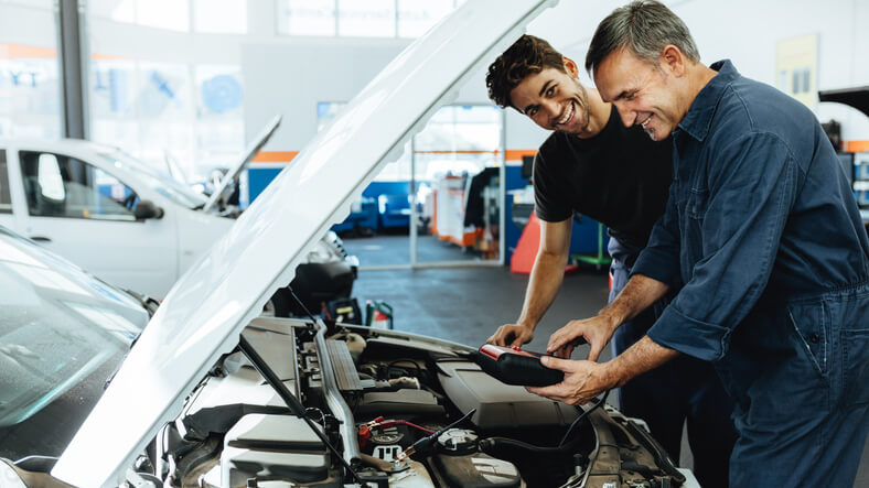 An experienced male auto mechanic instructing an apprentice during auto mechanic training