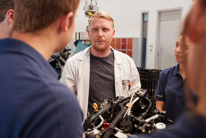 A group of budding auto mechanics receiving instructions from an instructor at our automotive school